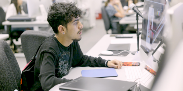 Pre-college student sits at computer working on graphic design project.